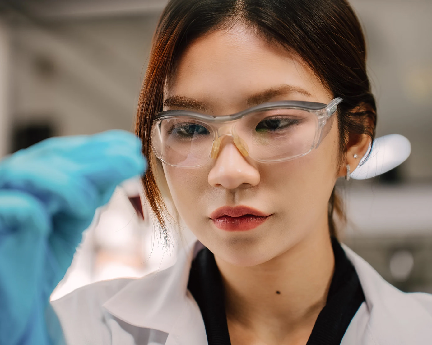 Close up, front view, of a female scientist holding a tube filled with blood, inspecting it at eye level.