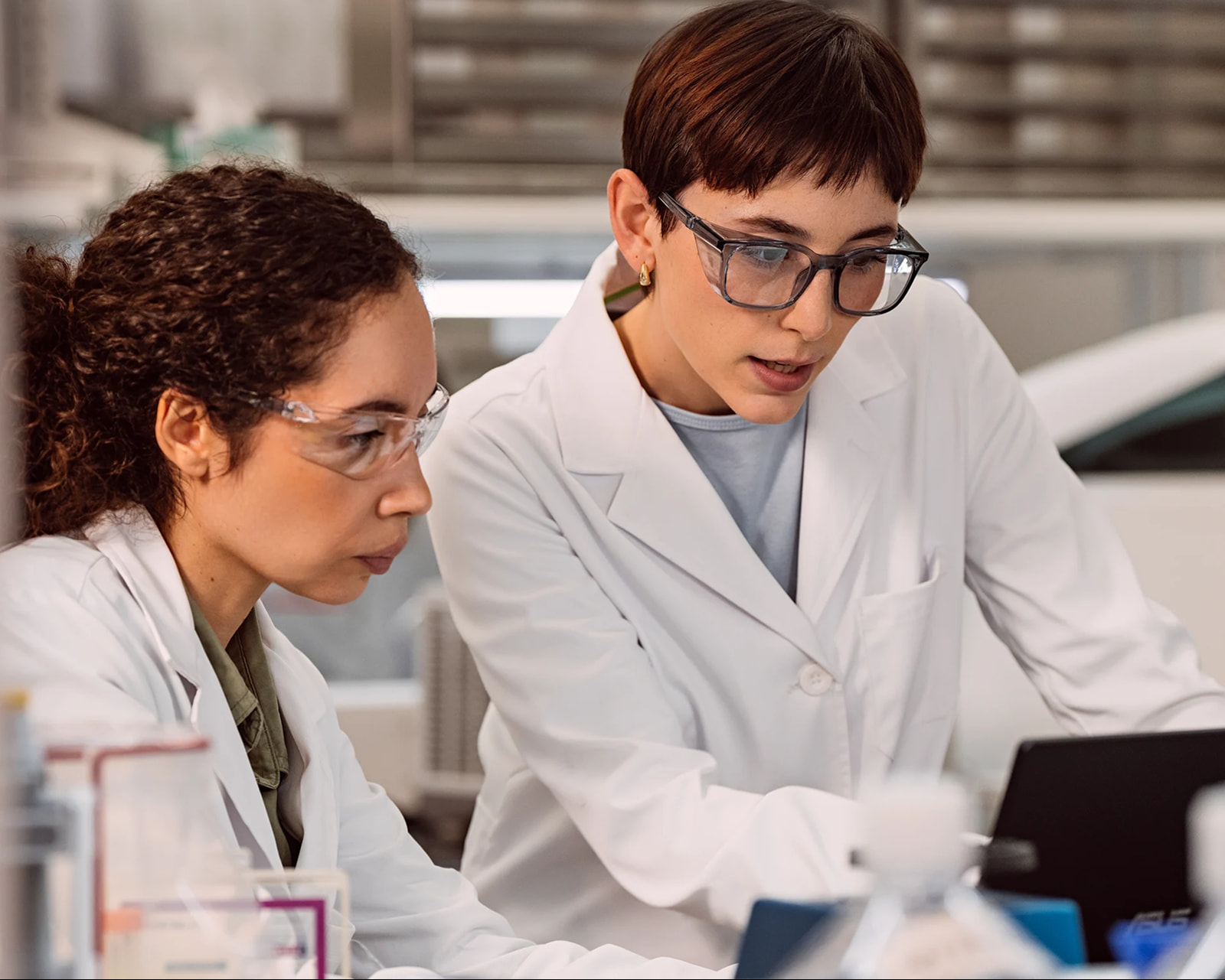 Two female scientists are working together, looking down at a monitor on a laptop in a lab setting.