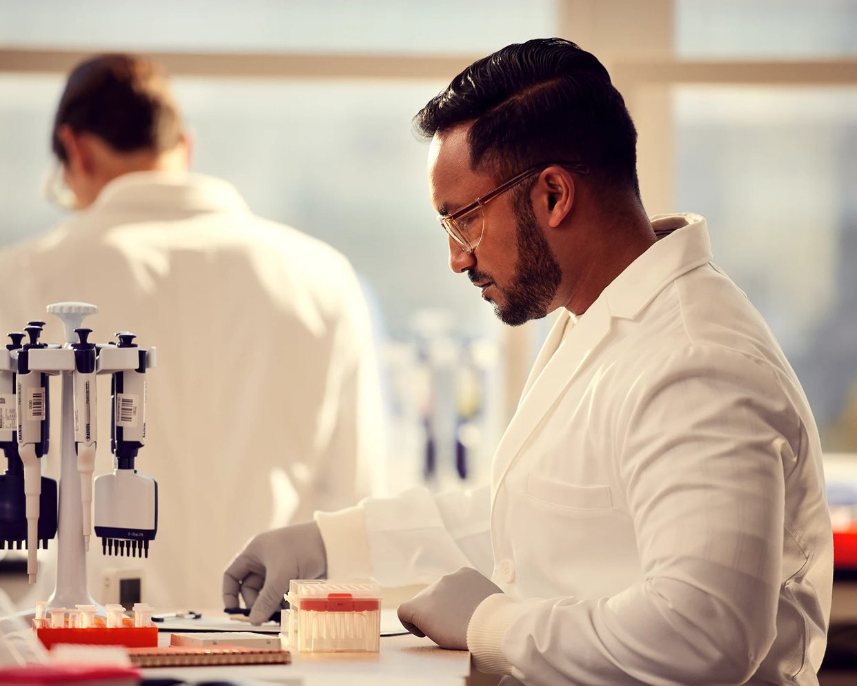 Male scientist, side view, preparing to write information on lab bench, other scientist blurry in background